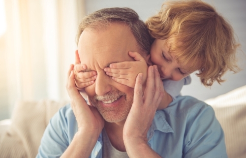 Middle aged man with his eyes covered by a small boy