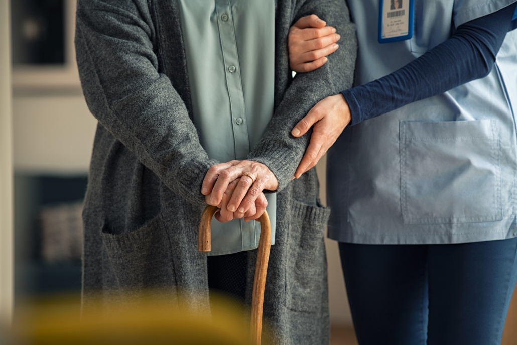 Nurse assisting an elderly person with a cane