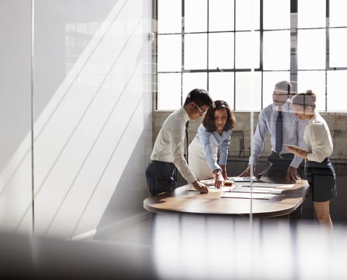 Four business colleagues stand talking in a meeting room