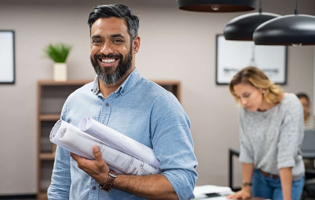 Architect smiles at the camera with plans rolled up in one arm