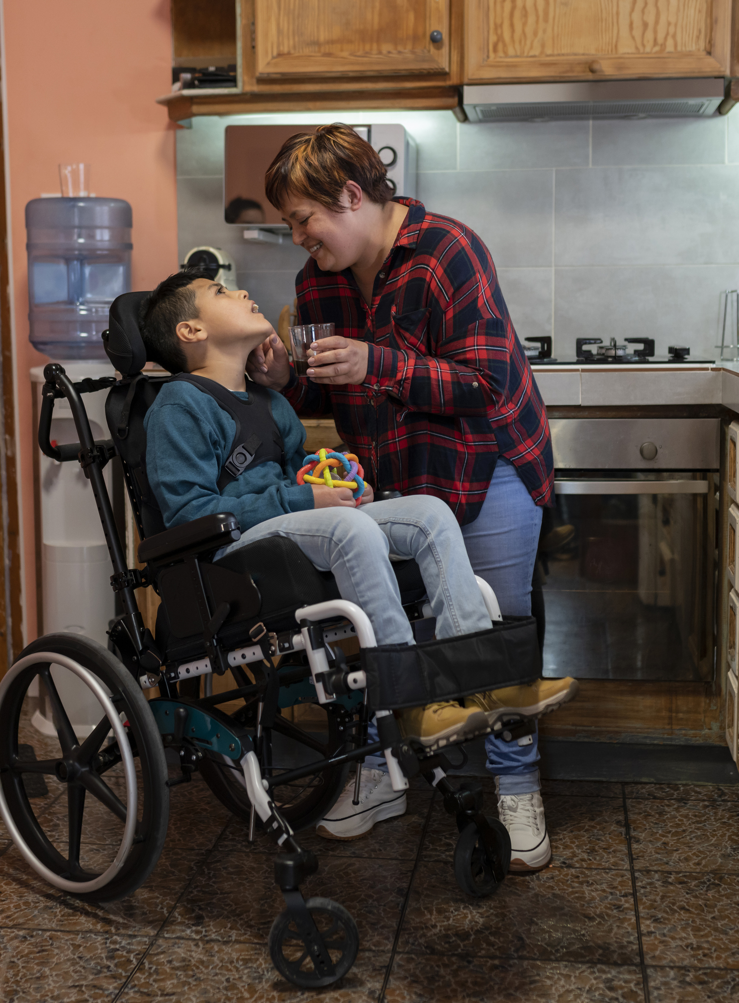 Mother caring for her wheelchair-bound disabled son in the kitchen.