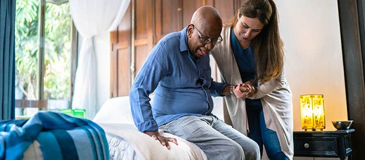 Home caregiver helping a senior man standing up at home