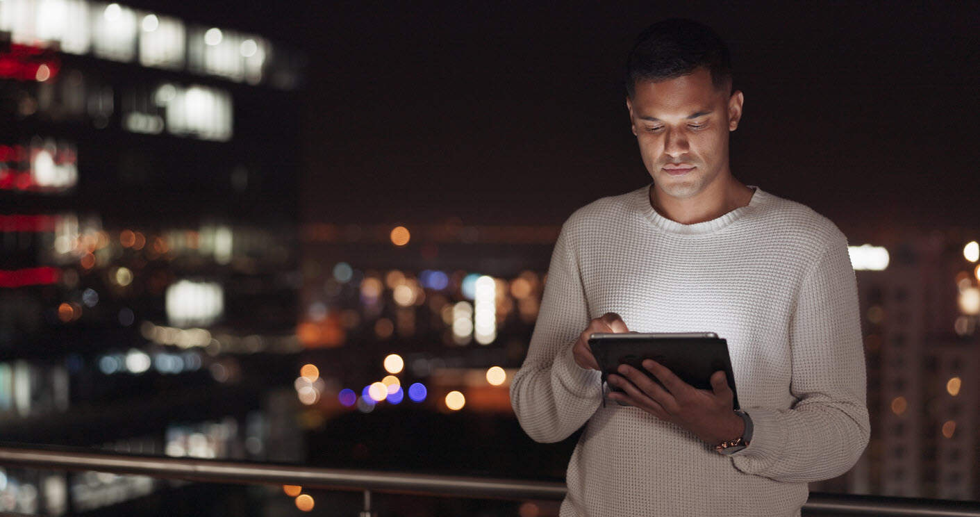 man scrolls on tablet with city in background