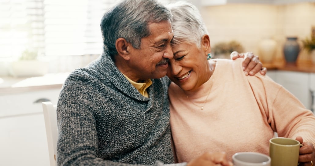 Hug, smile and senior couple with coffee, home and bonding with beverage in kitchen, people and morning. Happy, old man and mature woman with tea in house, comfortable and conversation for family